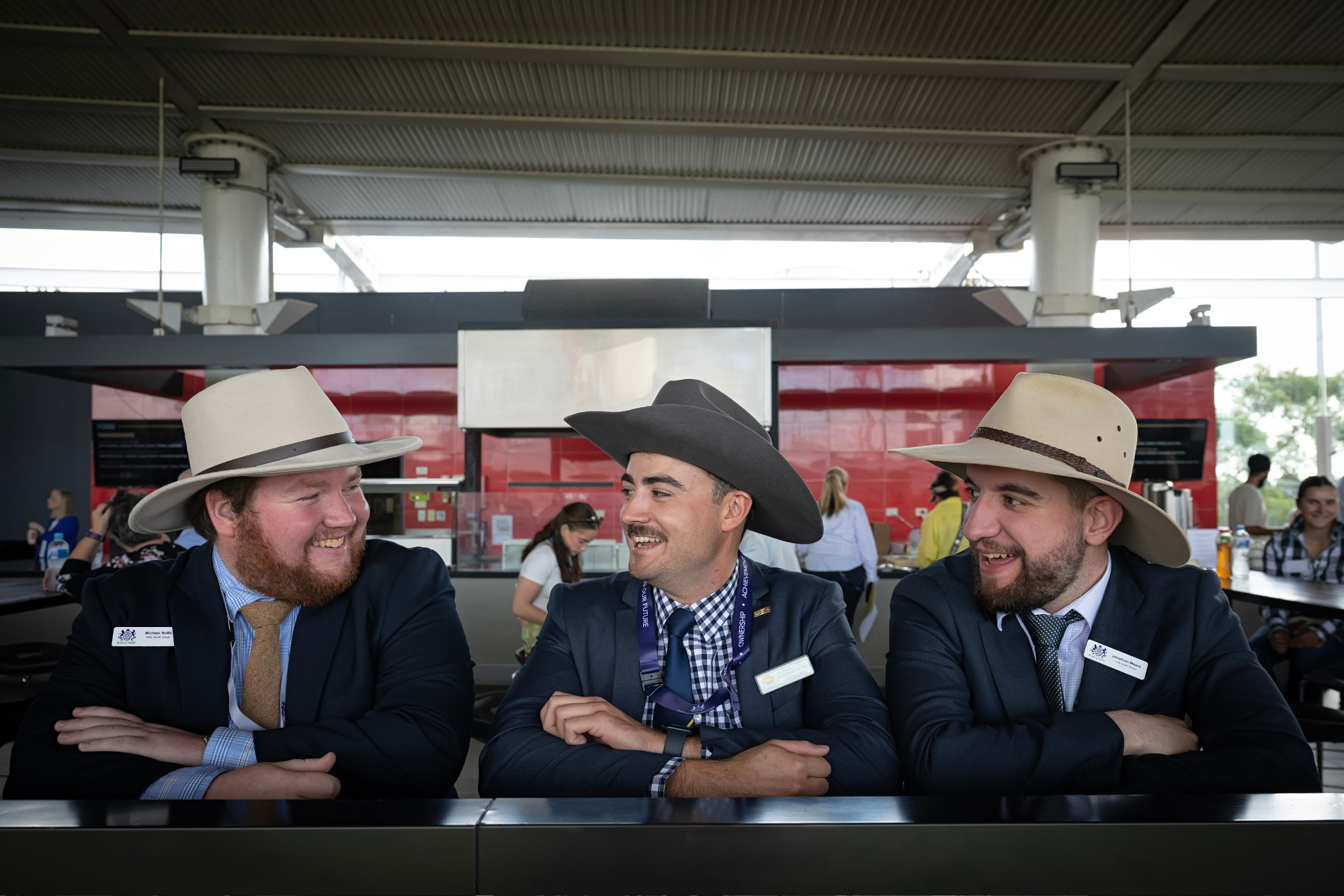 Three men in suits and wide-brimmed hats smiling and talking together at ENGIE Stadium.