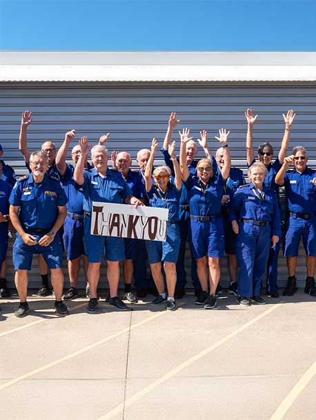 Group in blue uniforms raising hands and holding a “thank you” sign outdoors.