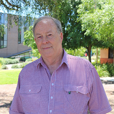 Headshot of RASF Board Member Jim Pratley standing outdoors in a red check shirt, with greenery and buildings in the background.