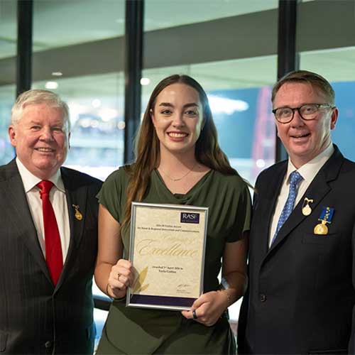 JB Fairfax Award recipient Tayla Gofton, a young brunette woman, smiling and holding a Certificate of Excellence with John Bennett and Michael Millner.