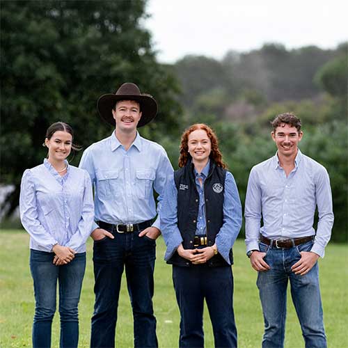 Four young adults - the RAS Foundation Rural Scholarship recipients - standing on grass in rural setting, wearing casual work wear.