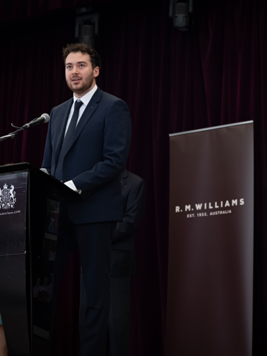 JB Fairfax Award 2025 winner Nick Newling in a dark suit, speaking at a podium in front of RAS Foundation banners.