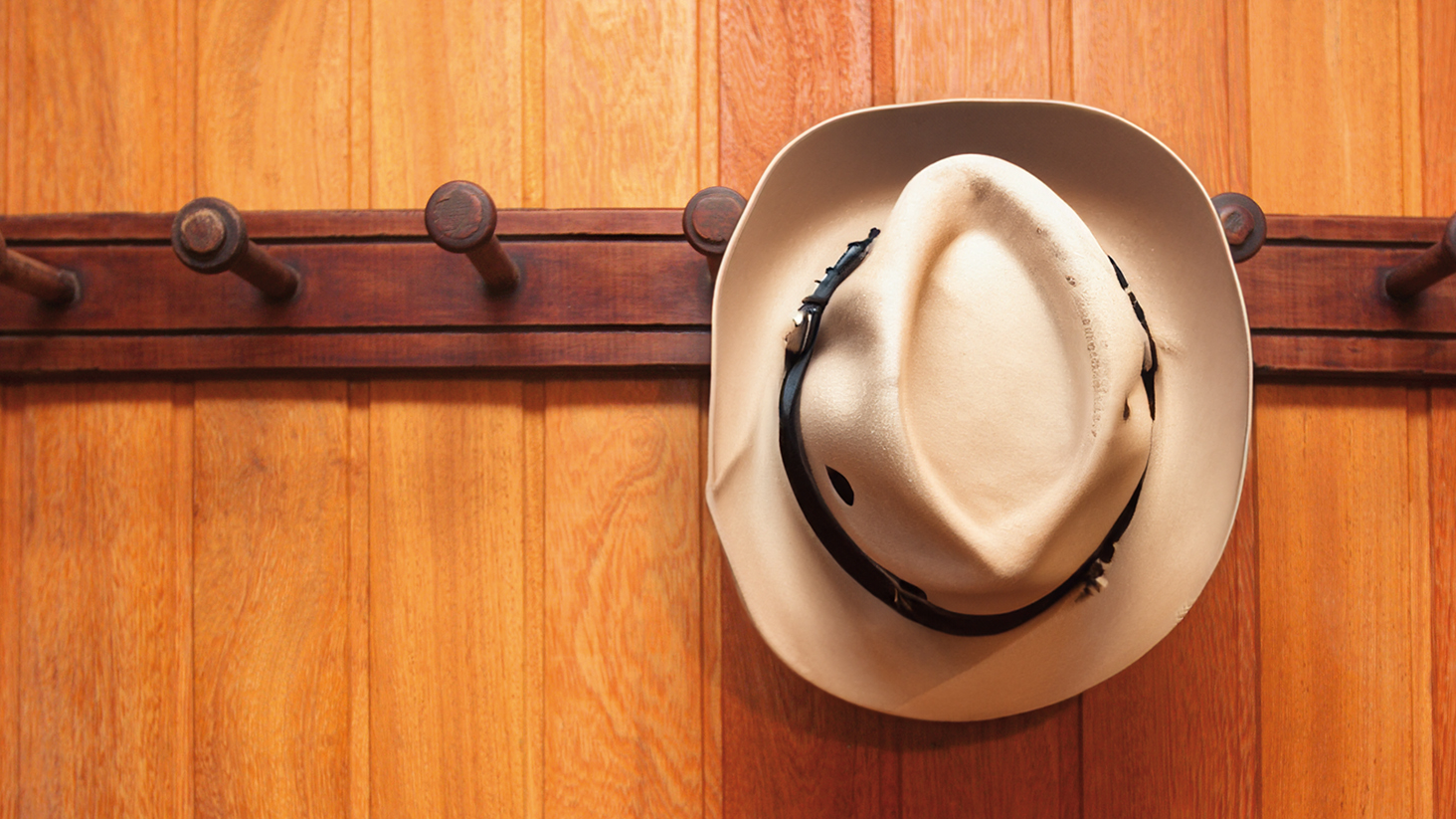 Beige stockman’s hat hanging on a wooden rack against a timber wall.