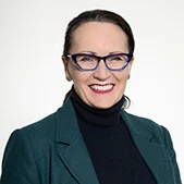 Headshot of Dairy Produce Chair Heidi Badgery, smiling and wearing glasses and a dark green jacket over a black top.