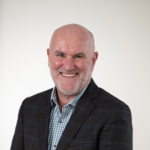 Headshot of Fine Food Committee Chair Michael Bullen, smiling and wearing a dark checked jacket and blue patterned shirt.
