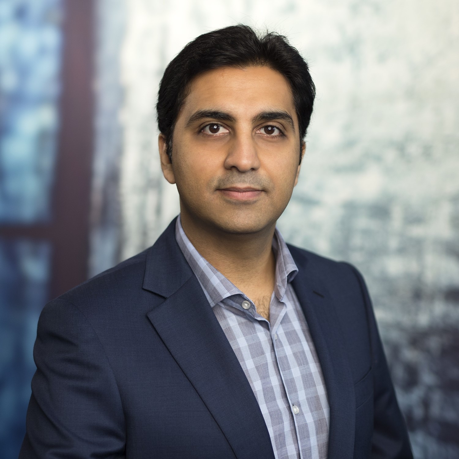 Headshot of Finance & Administration General Manager Zain Hoosen wearing a dark suit over a checked shirt.