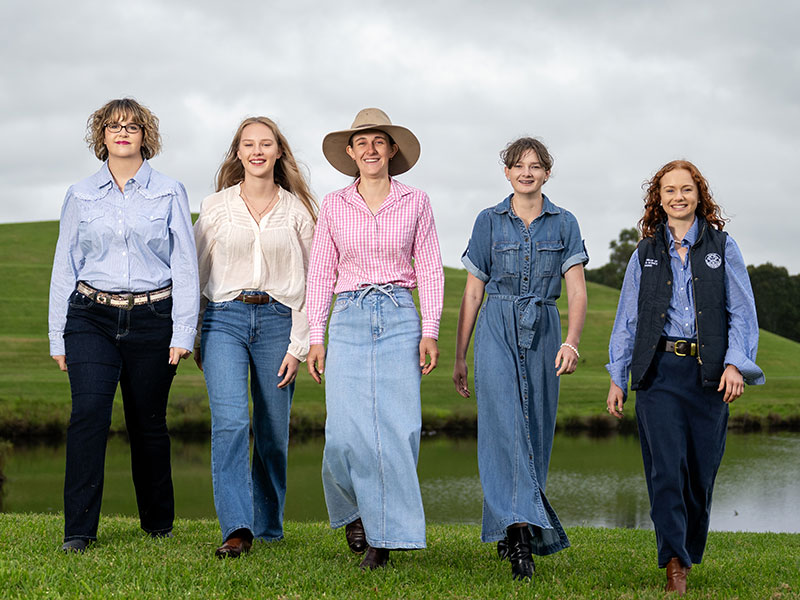 Five young women smiling and walking towards the camera in the middle of a green field with a lake backdrop, recipients of the 2026 RAS Foundation Rural Scholarship.