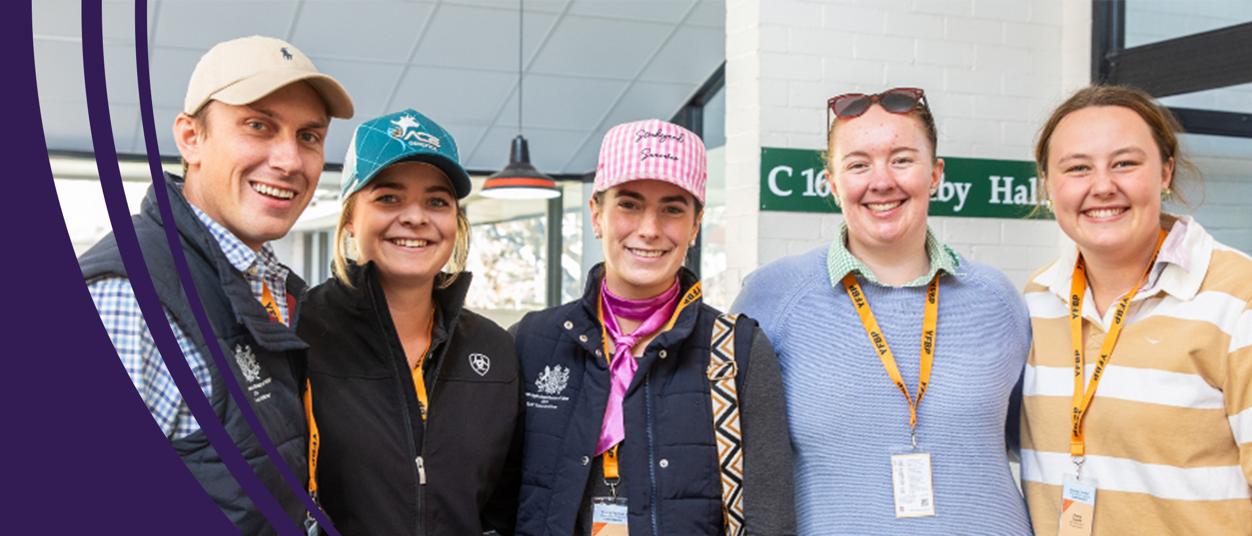 Five smiling agricultural workers wearing caps and lanyards stand together indoors, dressed in casual and workwear clothing.