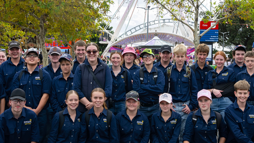 A group of high school students in matching navy shirts pose together outdoors at the Sydney Royal Easter Show.