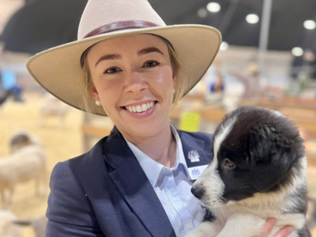 RAS Youth Group member Sarah Stanbury in a wide-brimmed hat and blazer, holding a black and white puppy in a show ring.