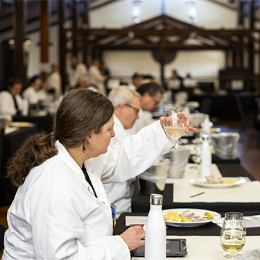 A wine judge in a white coat examines a glass of wine during a tasting session at a Sydney Royal Wine Competition.