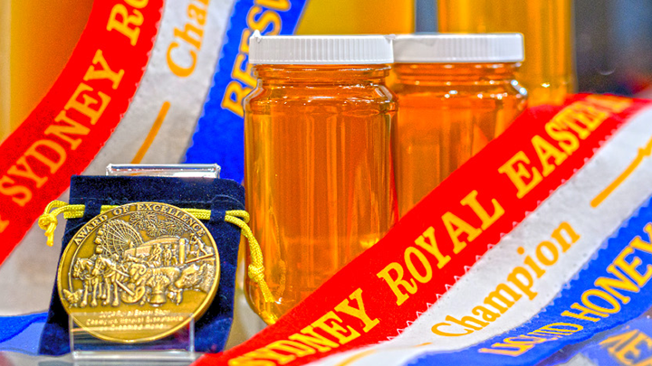 Two jars of honey with award ribbons and a gold medal of excellence displayed at the Sydney Royal National Honey Show.