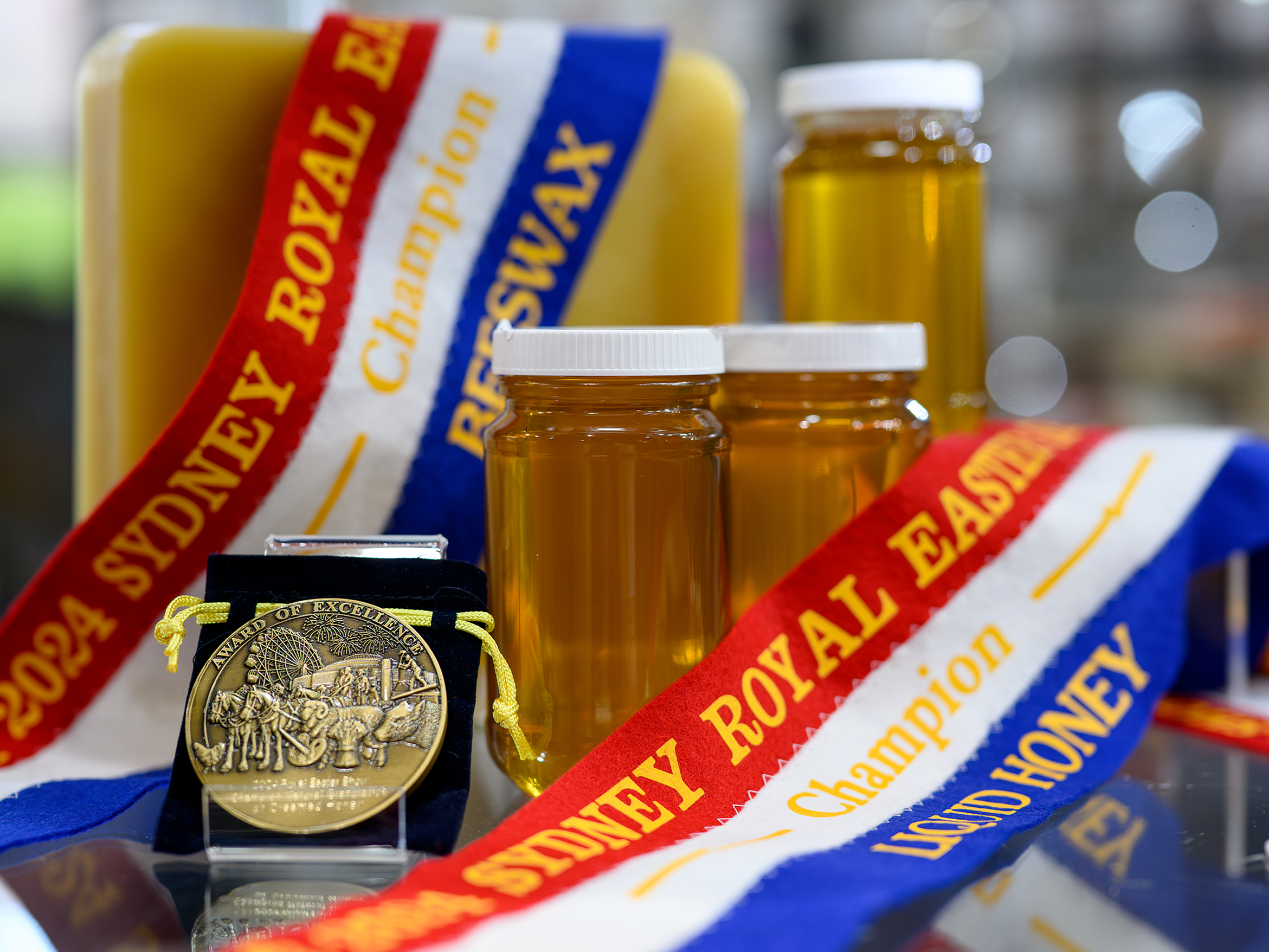 Two jars of honey with award ribbons and a gold medal of excellence displayed at the Sydney Royal National Honey Show.