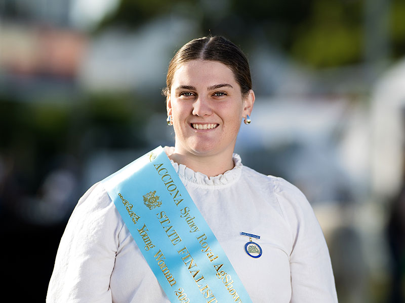 Headshot of 2026 Young Woman finalist Faith Greer, a brunette woman with hair pulled back, wearing a white shirt and a light blue sash.