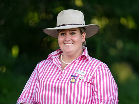 Headshot of 2025 finalist Claudia Williams, a woman with blonde hair, smiling, wearing a pearl necklace and a wide-brimmed hat.
