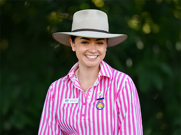 Headshot of Ninoska Birchall, a dark-haired woman wearing a pearl necklace, earrings, and a wide-brimmed hat.