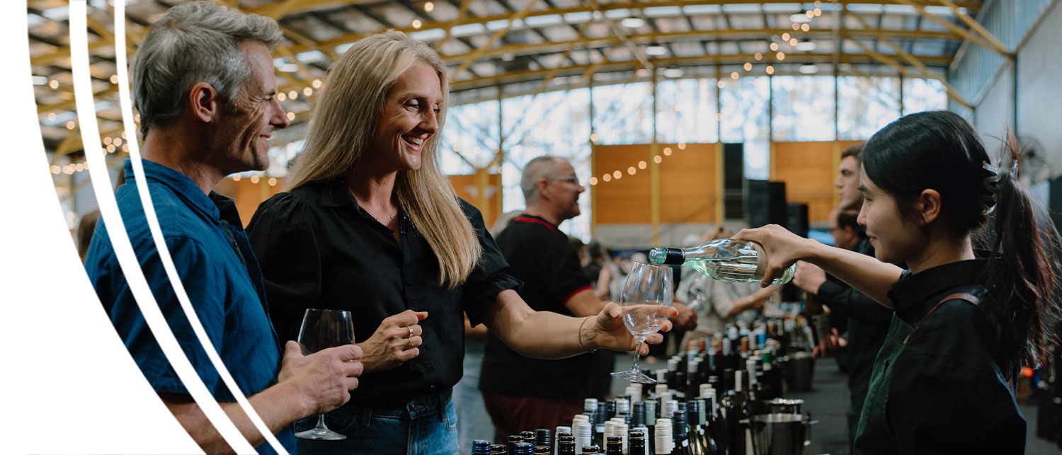 An older woman and her partner served white wine by a waitress in black clothes at the Grape Grain and Graze Festival.