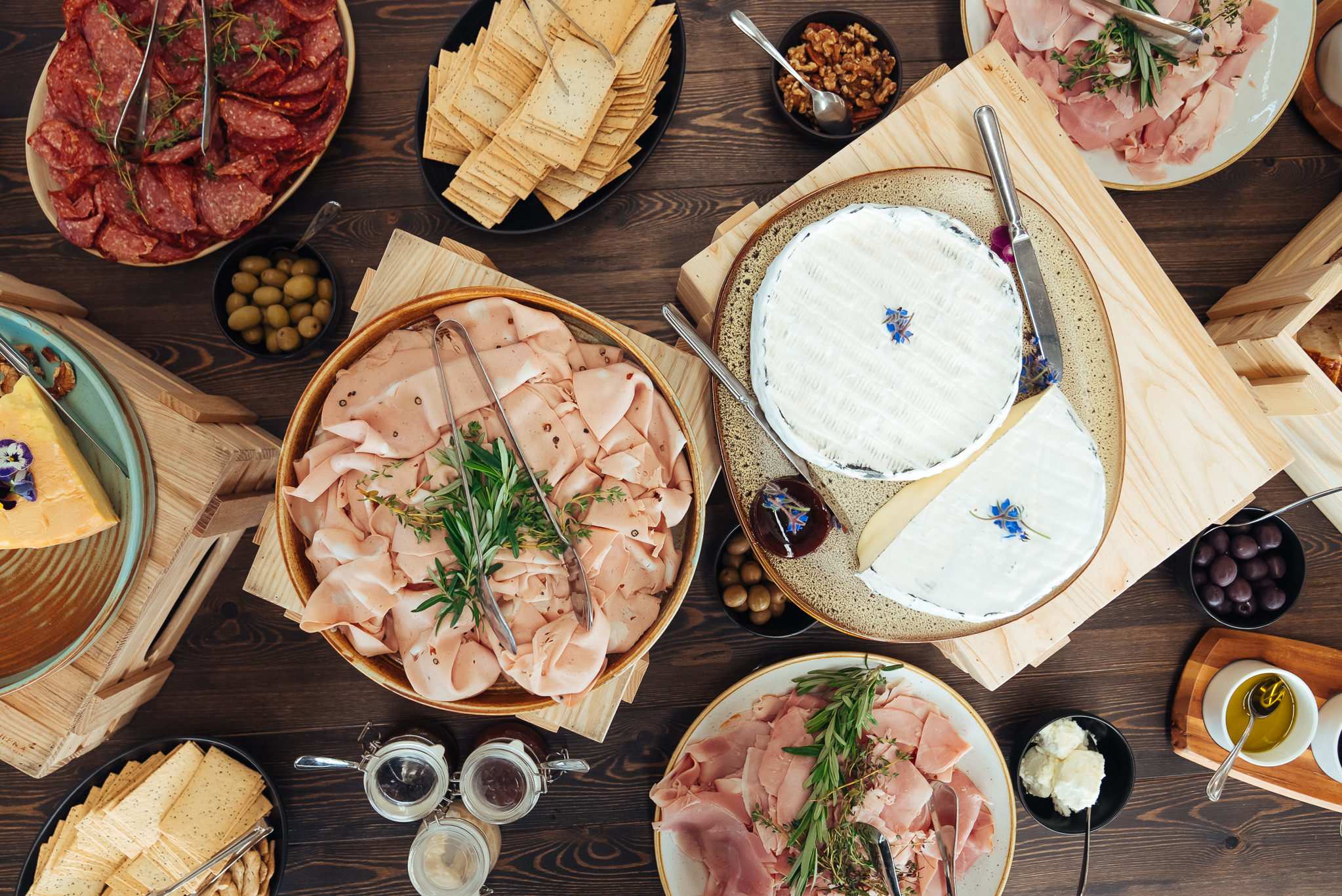 An assortment of cheeses, crackers, olives, nuts, and cured meat, paired with rosemary garnish and silver cutlery.