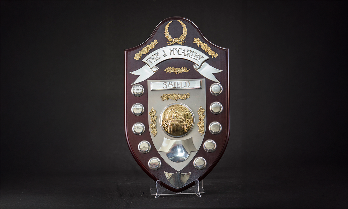 A shield shaped wooden plaque with silver and gold plates. The etched gold medallion in the centre depicts a winegrower in their cellar. Awarded since 1951.