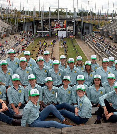 A group of high school students in matching green shirts  and caps pose together outdoors at Sydney Royal Easter Show's Woodchop Pavilion.
