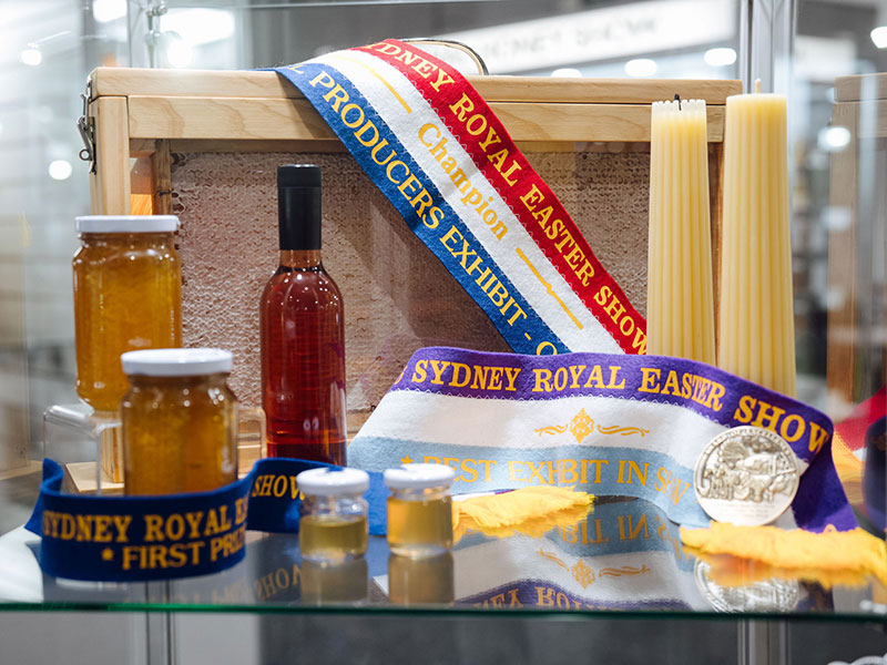 An assorted display of jarred honey, mead wax candles and honeycomb with champion ribbons at the Sydney Royal National Honey Show.